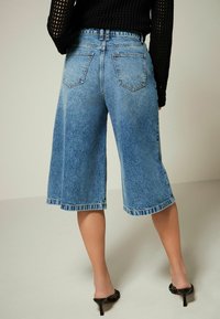 Culottes en denim bleu à coupe ample, ourlet effiloché et design cinq poches, avec une taille mi-haute et une texture délavée.
