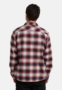 Camicia a maniche lunghe a quadratini nei colori rosso, blu navy e crema; presenta un colletto button-down e una vestibilità ampia con orlo curvo.