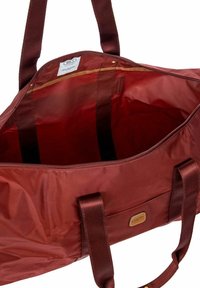 Sac fourre-tout en nylon rouge avec fermeture éclair, doté de deux poignées en tissu, d'une poche intérieure et d'une texture lisse. Doublé d'une couleur contrastante.