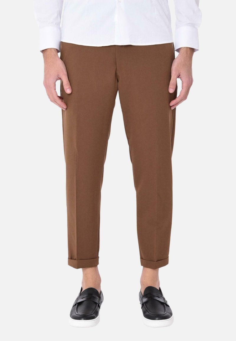 Pantaloni in cotone marroni con una vestibilità affusolata, con orli arrotolati; abbinati a scarpe nere senza lacci e a una camicia bianca con colletto.