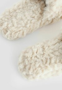 Pantofole in pelliccia sintetica di colore beige chiaro, caratterizzate da una texture morbida e pelosa e da una forma arrotondata, progettate per comfort e calore.