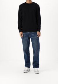 Maglietta nera a maniche lunghe con colletto a coste, abbinata a jeans di denim azzurro chiaro e sneakers bianche. Look casual e vestibilità rilassata.