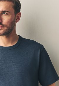Námornícky modré bavlnené tričko s kruhovým výstrihom, krátkymi rukávmi a hladkou textúrou. Jednoduchý dizajn bez viditeľných vzorov alebo grafiky.