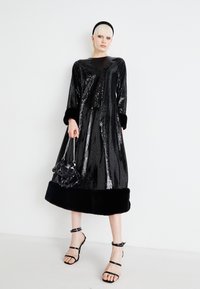 Črna obleka s sequinci in žametnim robom, dolgi rokavi in manšete. Usklajena z torbico z biseri in sandali z visoko peto.