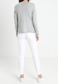 Camisa de manga larga gris hecha de una tela ligera, combinada con jeans blancos ajustados y zapatillas blancas. Diseño simple, sin patrones o elementos metálicos visibles.