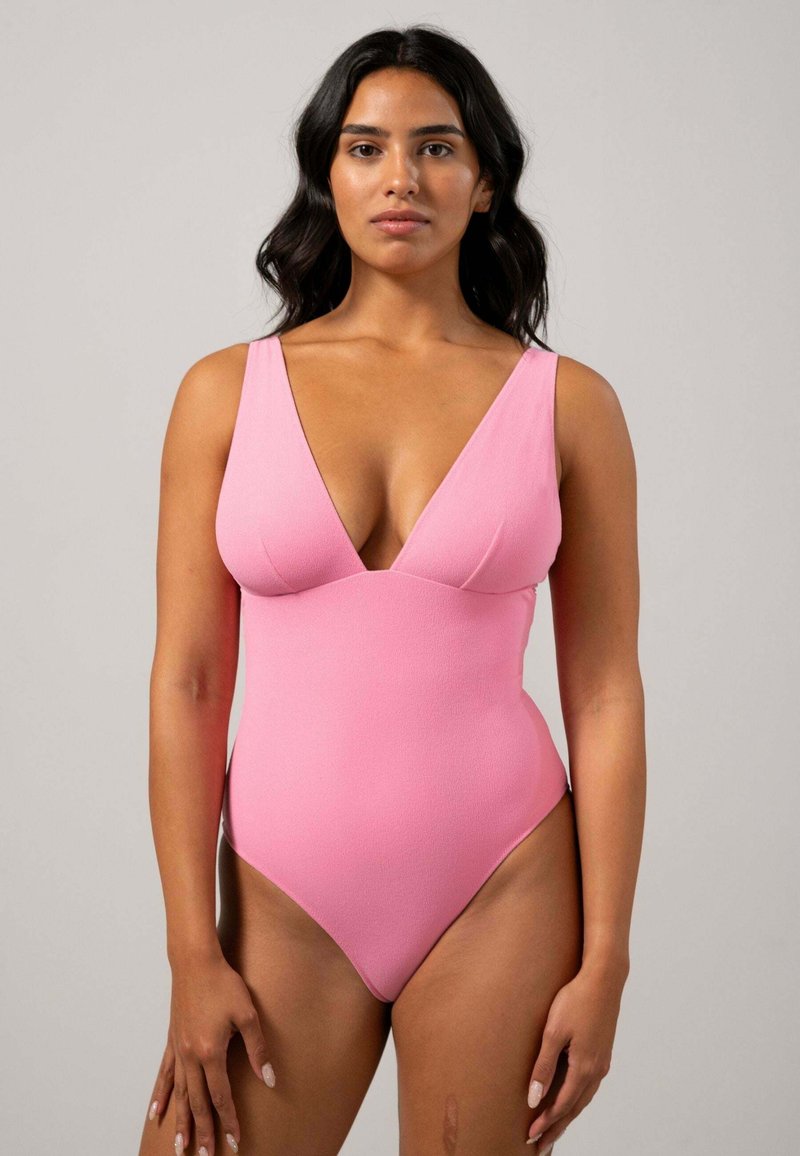 Roze badpak met een diepe V-halslijn, brede schouderbanden en een gladde textuur; hoge beenopeningen. Eenvoudig en strak ontwerp.