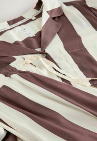 Hemd mit Knöpfen, das breite vertikale Streifen in Braun und Creme zeigt. Weicher Stoff, mit Kragen, Tasche und einem Kordelzug-Detail in der Taille.