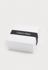 Valge ruutkarp, millel on must riba, millel on silt "Calvin Klein." Sujuv tekstuur, minimalistik disain, avaneb ülevalt.