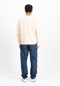 Beige sweatshirt med ribbede manchetter og kant, parret med blå denim jeans med baglommer og hvide sneakers. Simple og afslappet pasform.