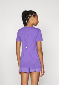 Purple athletic t-shirt with a fitted design, featuring a textured pattern and logo on the back. Paired with matching purple shorts.