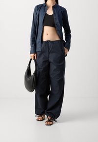 Navy knapplång skjorta, svart crop top, lösa navybyxor med dragsko och svart toteväska. Sandaler med tunna remmar och fyrkantiga tår.