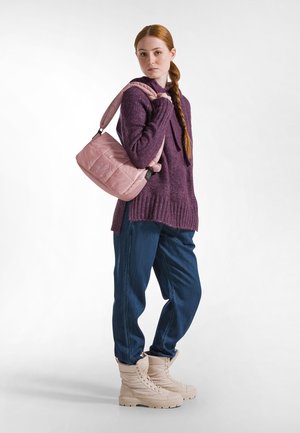 Borsa a spalla imbottita rosa con un accento arricciato, appesa a un modello che indossa un maglione viola scuro e jeans blu, completati da stivaletti beige.