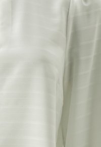 Blusa bianca con sottili righe orizzontali, realizzata in tessuto leggero, con una superficie liscia e maniche corte. Senza chiusure visibili.