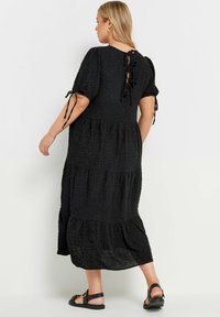 Svart lager-på-lager klänning med puffsleeves och snörningsdetalj bak. Texturerad tyg med en lös passform som når mitt på vaden. Matchad med platta sandaler.