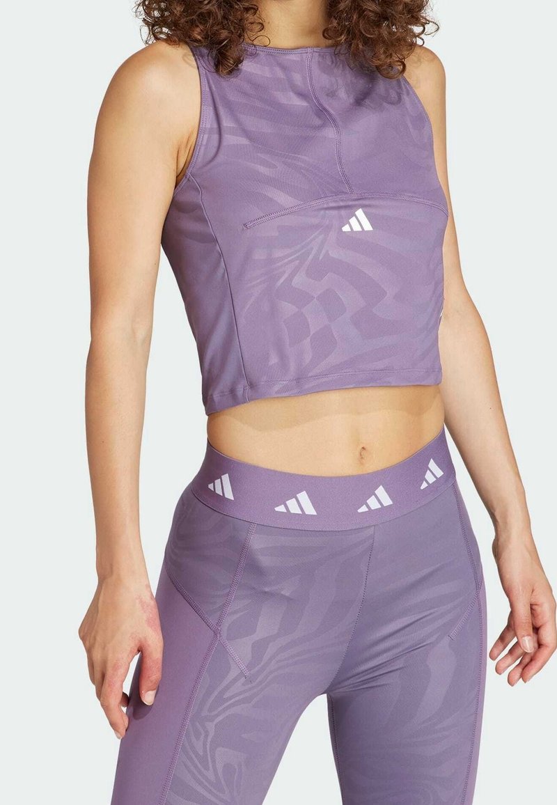 Top deportivo corto morado con diseño texturizado, que cuenta con un bolsillo frontal y un logo blanco. Combinado con mallas de talle alto a juego.