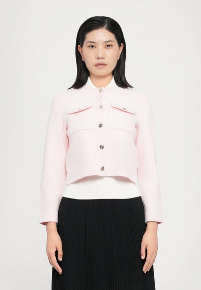 Helle rosa, kurz geschnittene Jacke mit langen Ärmeln, ausgestattet mit zwei Brusttaschen, silbernen Knöpfen und einem passenden weißen Kragen. Strukturierter Stoff mit sichtbaren Nähten.