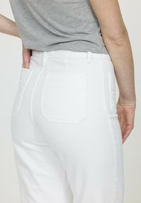 Pantalons en denim blanc à taille haute, dotés de deux poches arrière, d'une texture lisse et d'un design épuré. Vu de l'arrière.