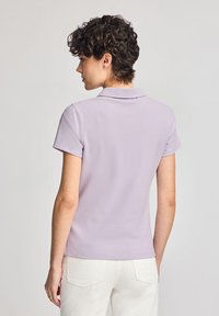 Ljuslila polo skjorta med krage och korta ärmar, tillverkad av mjukt material. Har en rak fåll och en minimalistisk design.