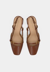 Chaussures slingback en cuir marron avec un bout carré, dotées de deux fines lanières et de boucles dorées. Doublure intérieure beige douce.