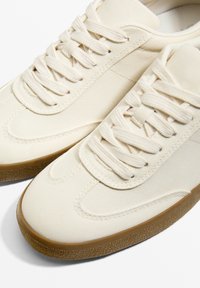 Canvas-Sneaker in Beige mit flachen Schnürsenkeln, Gummisohle und gesteppten Akzenten. Runde Zehenpartie mit strukturiertem Außensohle für besseren Halt.