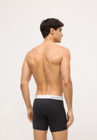 Fekete boxer alsónadrág geometrikus mintával, fehér logóval ellátott derékpánttal. Puha anyag, testhezálló kialakítás, combközép hosszuság, és minimalista varrások.