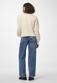 Κρεμ μαρινάκι πουλόβερ με ριγέ υφή, συνδυασμένο με ανοιχτό μπλε φαρδιά τζιν παντελόνια και μαύρες χοντρές μπότες.