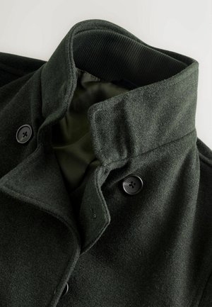 Tume roheline villa segu mantel kõrge kraega, mustade nuppudega ja sileda sisemise voodriga. Tekstureeritud kangas pehme viimistlusega.