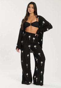 Cardigan aperto nero e pantaloni palazzo abbinati, caratterizzati da ricami bianchi di palme, abbinati a un top bikini nero. Tessuto morbido, vestibilità comoda.