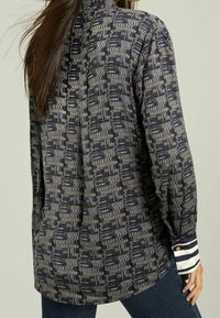 Camicia a maniche lunghe in tessuto blu navy con un motivo geometrico testurizzato. Presenta polsini a strisce a contrasto e una vestibilità comoda.