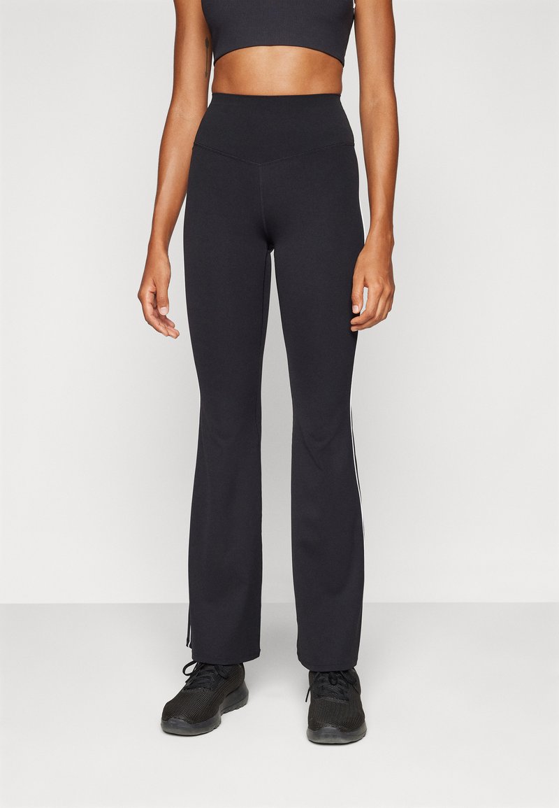 Black flared workout pants with a high waistband and white side stripes, made from stretchy fabric. Paired with black sneakers.