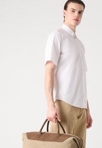 Camisa blanca de manga corta con cuello abotonado, combinada con pantalones beige. La persona lleva un gran bolso de tela y cuero marrón.