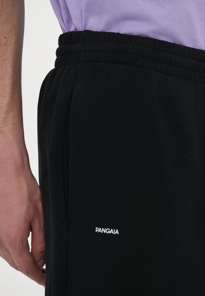 Pantalons de survêtement noirs avec une ceinture texturée et des poches latérales. Le nom de la marque "Pangaia" est brodé en blanc sur la cuisse gauche.