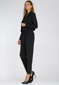 Czarna krótka marynarka na dopasowanym kombinezonie o gładkiej fakturze. Uzupełniona błyszczącymi czarnymi szpilkami.
