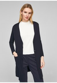 Lång marinblå kofta med öppen framsida, ribbat mönster, sidofickor och knäppningar. Bärs över en vit topp med scallopad nederkant.