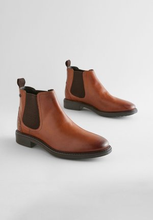 Cizme Chelsea din piele maro, cu panouri elastice pe laterale, vârf rotund și buclă pentru tragere. Prezintă o textură netedă și un toc jos și suprapus.