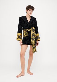 Schwarzer Samt-Robe mit einem strukturierten Logo-Muster, gelbgoldenen Akzenten an den Ärmeln und dem Gürtel sowie einem Schalkragen-Design.