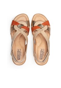 Sandalias marrones con diseño de tiras cruzadas, que presentan acentos en naranja y bronce metálico. Textura de cuero suave, plantilla acolchada con logotipo.