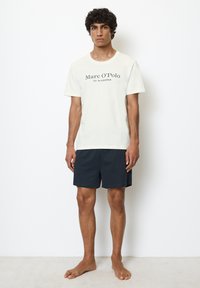 Hvid bomulds t-shirt med "Marc O'Polo" tekst, parret med marineblå shorts. Outfittet har en klassisk pasform og blød tekstur.