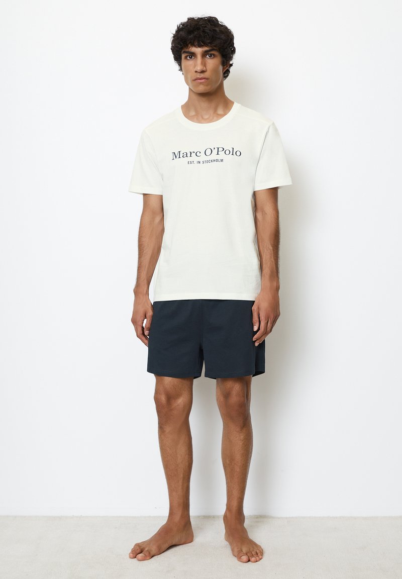 Hvid bomulds t-shirt med "Marc O'Polo" tekst, parret med marineblå shorts. Outfittet har en klassisk pasform og blød tekstur.