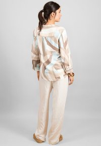 Blusa multicolore con strisce astratte beige e blu, tessuto leggero, maniche lunghe, abbinata a pantaloni di lino beige chiaro.