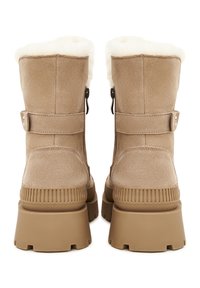 Paire de bottes d'hiver en daim beige avec semelles épaisses en caoutchouc et doublure en polaire blanche visible en haut, vue de dos.