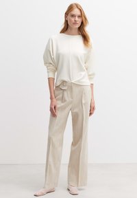 Helles Creme-Sweatshirt mit überschnittenen Schultern, kombiniert mit beigen, plissierten Hosen. Beide Kleidungsstücke bestehen aus einem weichen, strukturierten Stoff.