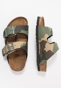 Sandali con motivo camouflage, dotati di due fibbie regolabili, soletta in sughero, suola in gomma e tomaia vegana testurizzata in tonalità verde e beige.
