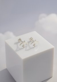 Silverfärgade fågelformade stiftörhängen på en glansig vit utställning. Har en polerad yta och bakdelar för säker användning.