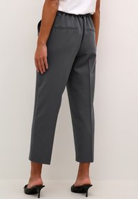 Pantalons gris taille haute avec une taille élastique, texture lisse, jambes fuselées et deux poches arrières, associés à des sandales noires à talons.