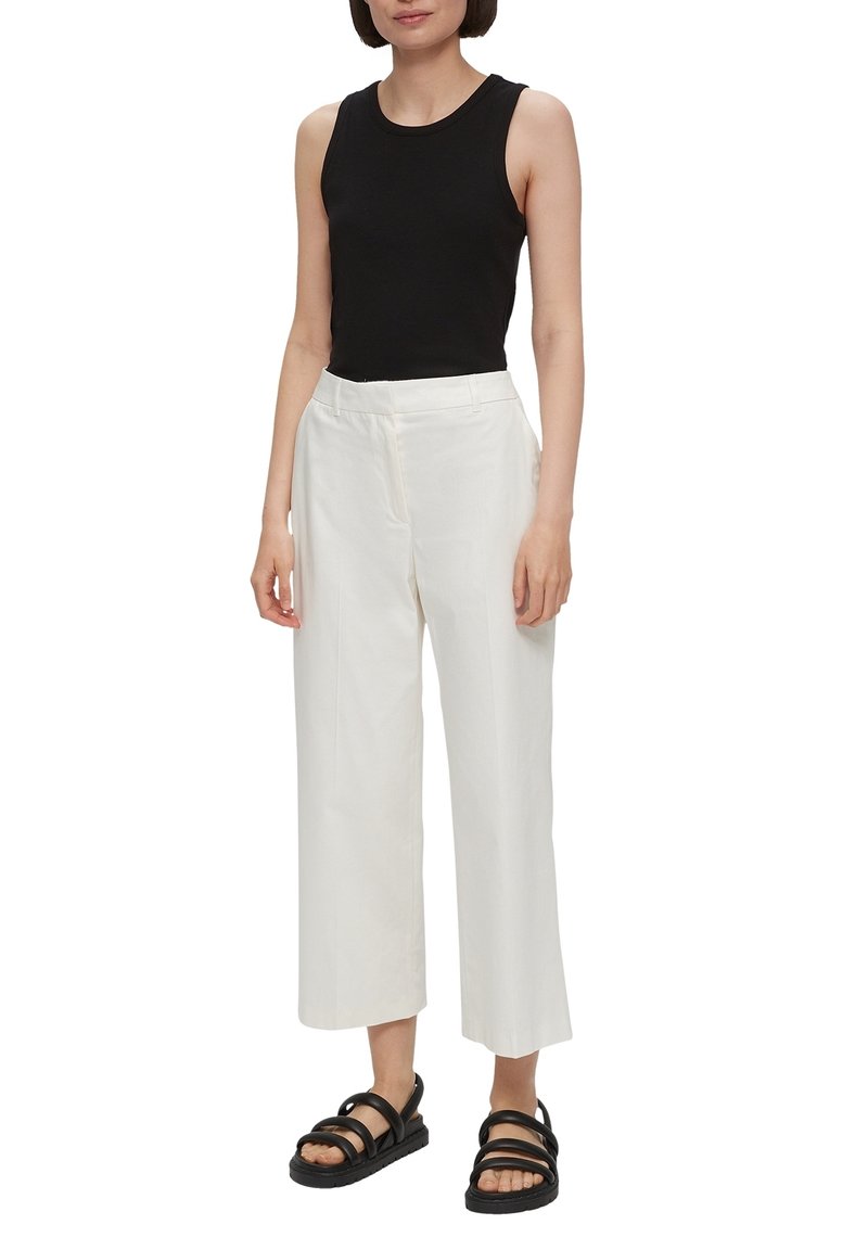 Top sans manches noir, pantalon large blanc, et sandales noires à lanières. Tissu en coton, coupe décontractée, design minimaliste, sans motifs.