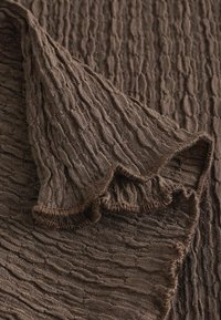 Tissu marron tricoté avec un motif texturé ondulé et un bord doux légèrement plié montrant les détails du tricot.