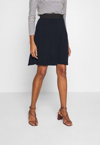 Černá sukně ke kolenům s elastickým pasem, doplněná pruhovaným topem s dlouhým rukávem. Modelka má na sobě bordó sandály na podpatku se zavazováním.