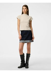 Top beige a maniche corte con collo alto, abbinato a una mini gonna in jeans scuri con orlo in jeans chiari e tasche. Stivali neri fino al ginocchio.