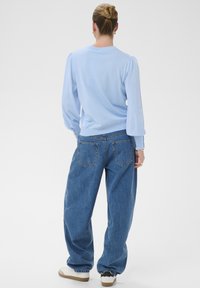Haut à manches longues bleu clair avec épaules bouffantes, associé à un jean en denim bleu ample avec poches arrière et coupe droite.